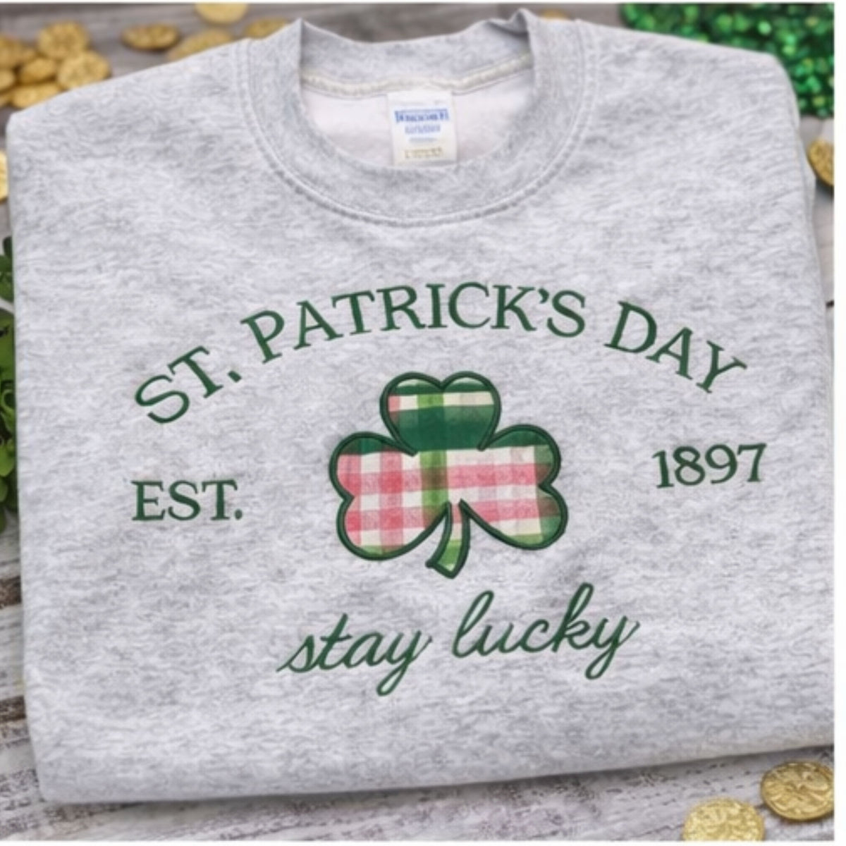 Gray sweatshirt with St. Patrick's Day design featuring a shamrock and text on a wooden surface.