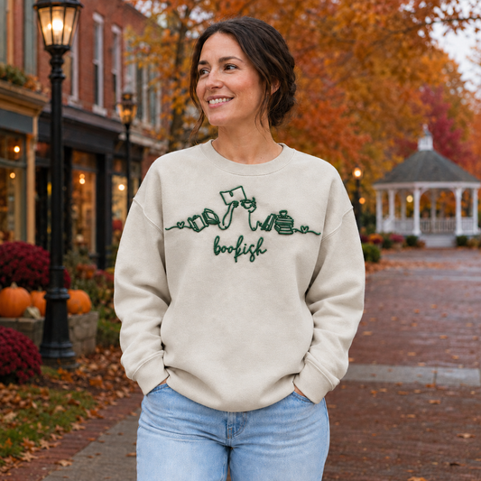 Bookish reader machine embroidery centered on a Sand Gildan Softstyle sweatshirt, approximately 10 inches wide