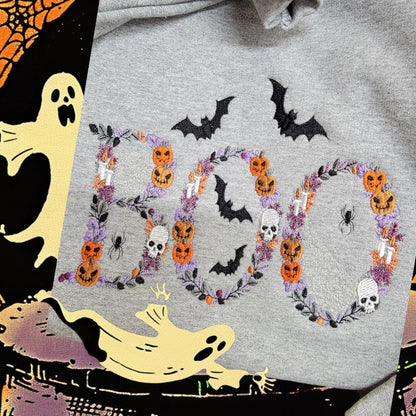 Close-up of Botanical BOO embroidery with pumpkins, skulls, candles, bats and florals on an Ash sweatshirt