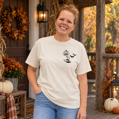 Woman wearing an Ivory Comfort Colors-style tee with black pumpkin, witch hat, and bats embroidery on the left chest.