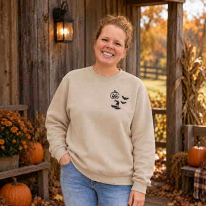 Woman wearing a Sand crewneck sweatshirt with black pumpkin, witch hat, and bats embroidery on the left chest.