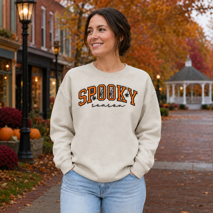 Adult woman wearing a Sand Spooky Season sweatshirt with orange black and white center-chest embroidery
