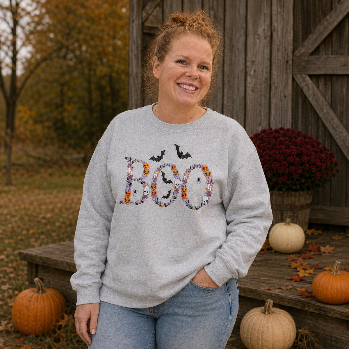 Woman wearing an Ash Botanical BOO embroidered Halloween sweatshirt in a rustic fall setting