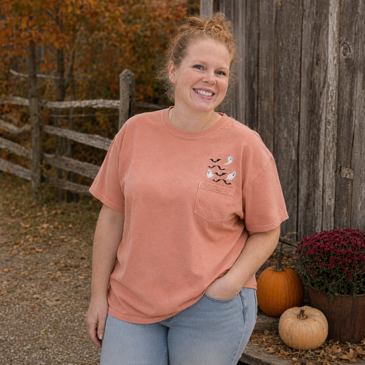 Woman wearing a Terracotta Comfort Colors pocket T-shirt with embroidered white ghosts and black bats in a fall setting