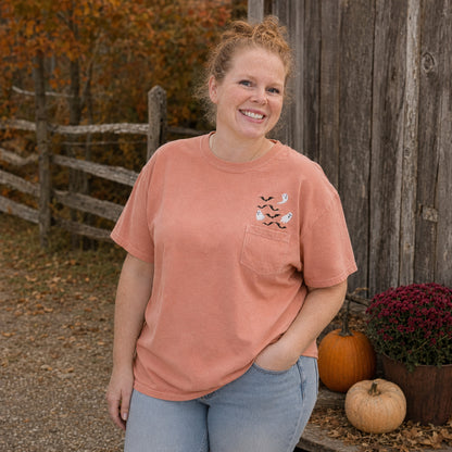 Woman wearing a Terracotta Comfort Colors pocket T-shirt with embroidered white ghosts and black bats in a fall setting