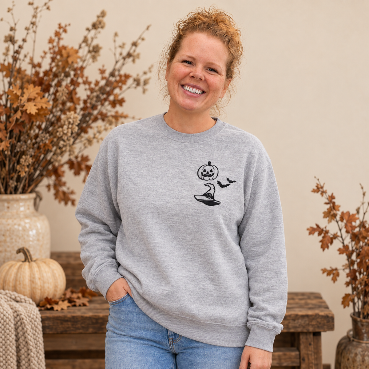 Woman wearing an Ash grey embroidered Halloween sweatshirt with a small black left-chest design.