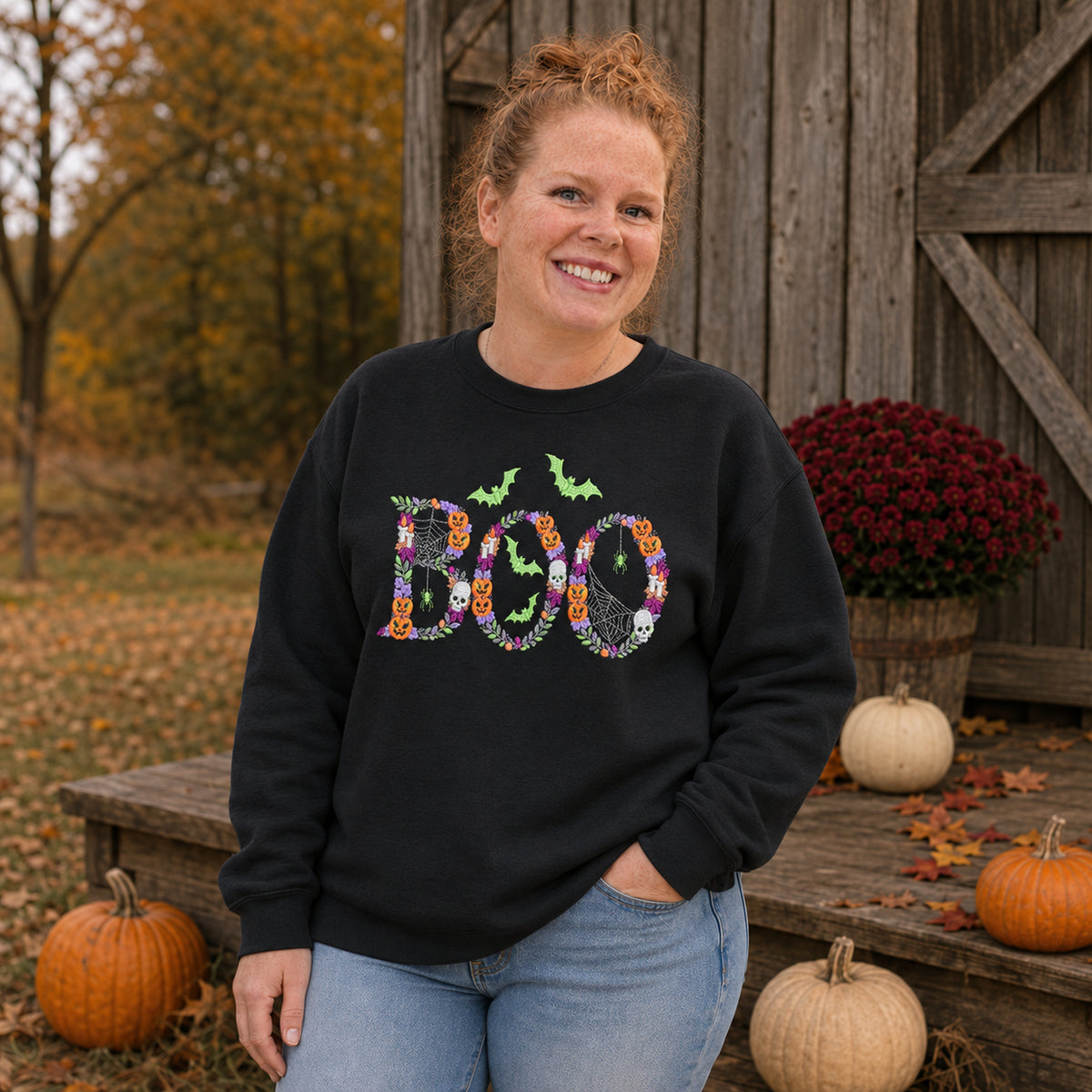 Woman wearing a Black Botanical BOO embroidered Halloween sweatshirt on a rustic autumn porch