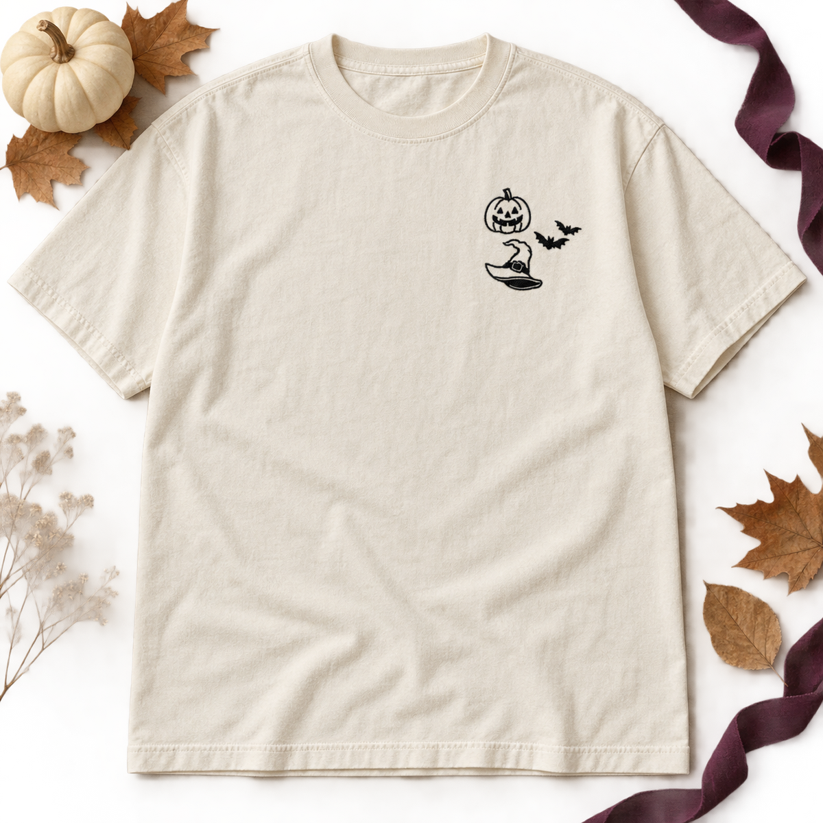 Ivory heavyweight T-shirt flat lay with black jack-o-lantern, two bats, and witch hat embroidery.
