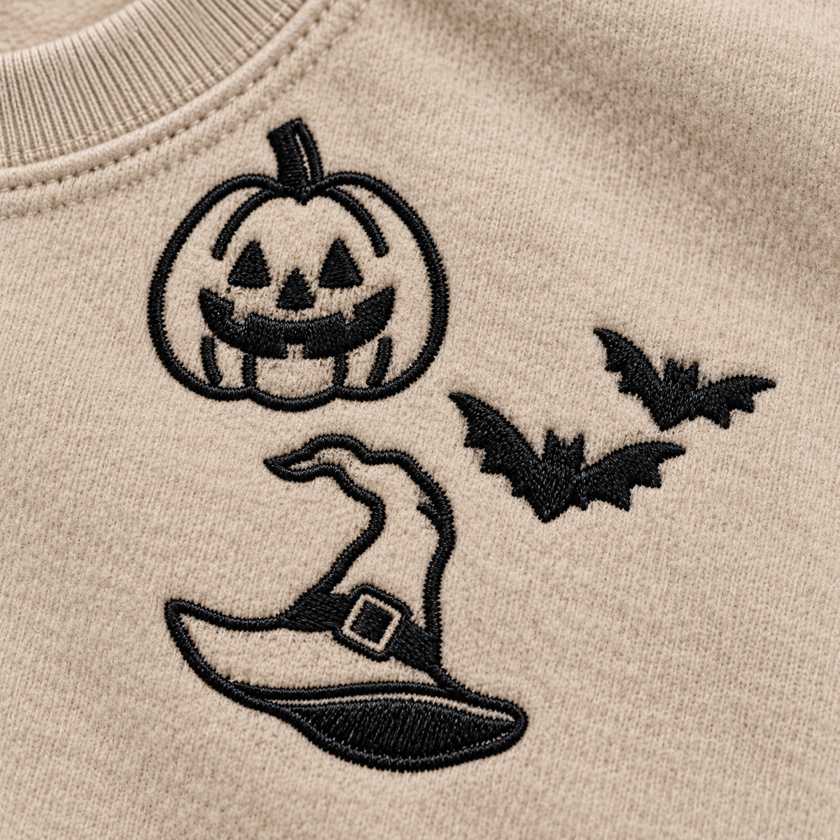 Close-up of black pumpkin, bats, and witch hat machine embroidery on Sand sweatshirt fleece.