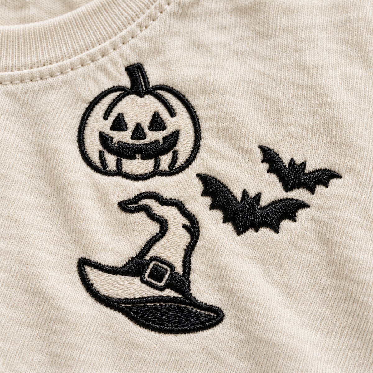 Close-up of black pumpkin, bats, and witch hat machine embroidery on Ivory cotton.