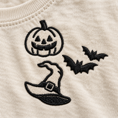 Close-up of black pumpkin, bats, and witch hat machine embroidery on Ivory cotton.