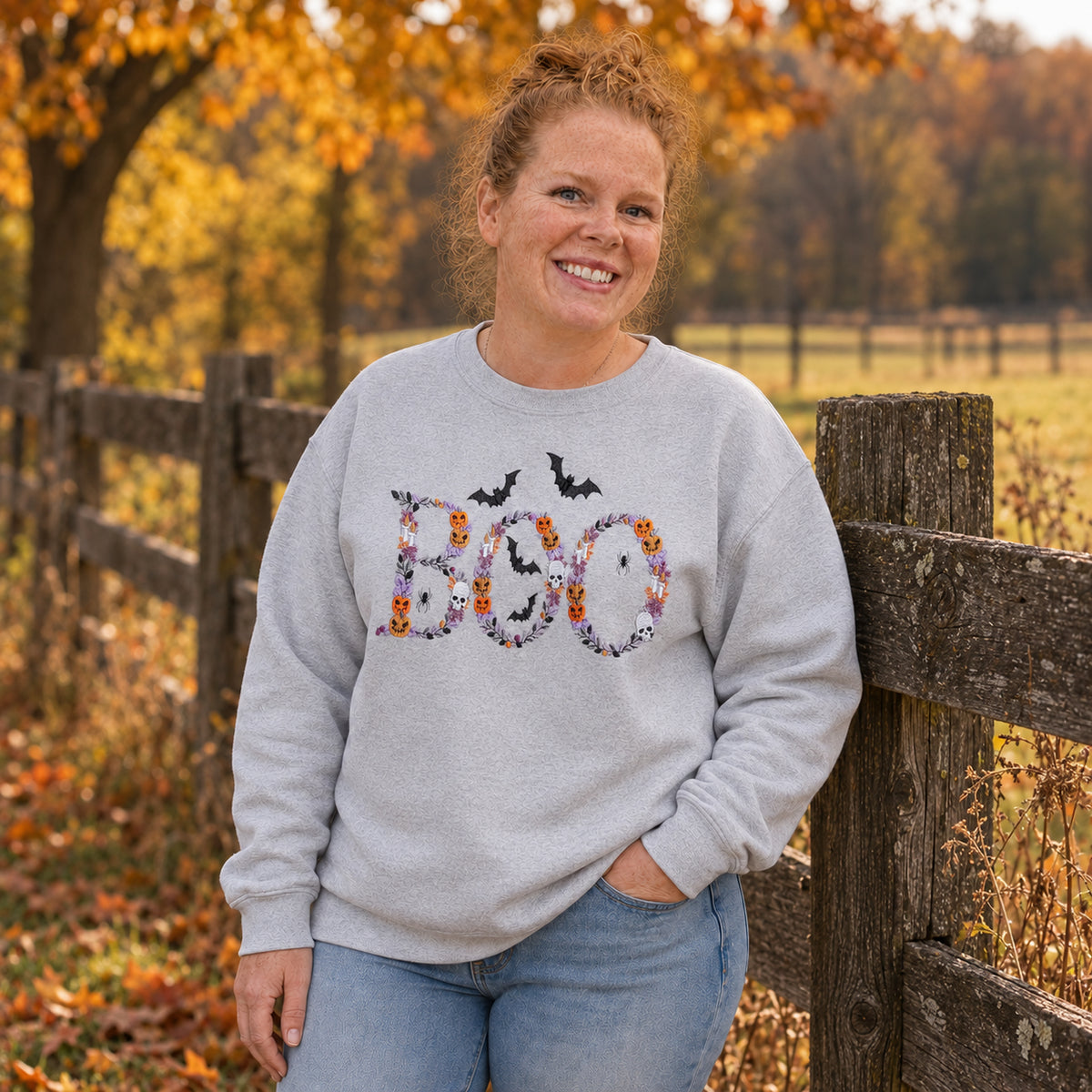 Woman wearing an Ash Botanical BOO embroidered Halloween crewneck beside a farm fence in autumn