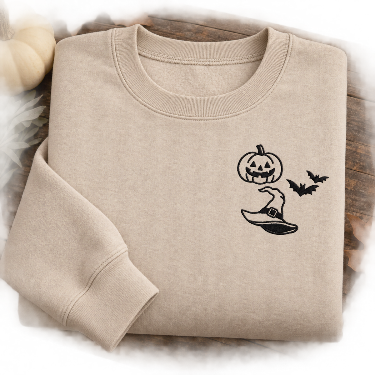 Folded Sand Halloween sweatshirt displaying black pumpkin, bats, and witch hat embroidery.