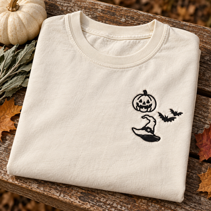 Folded Ivory Halloween T-shirt displaying black pumpkin, bats, and witch hat embroidery.