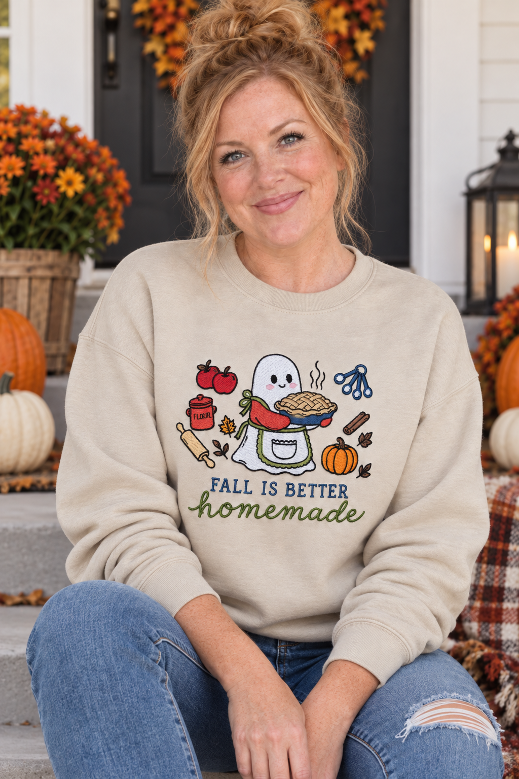 Woman seated on a fall porch wearing a Sand Fall Is Better Homemade embroidered ghost baker sweatshirt