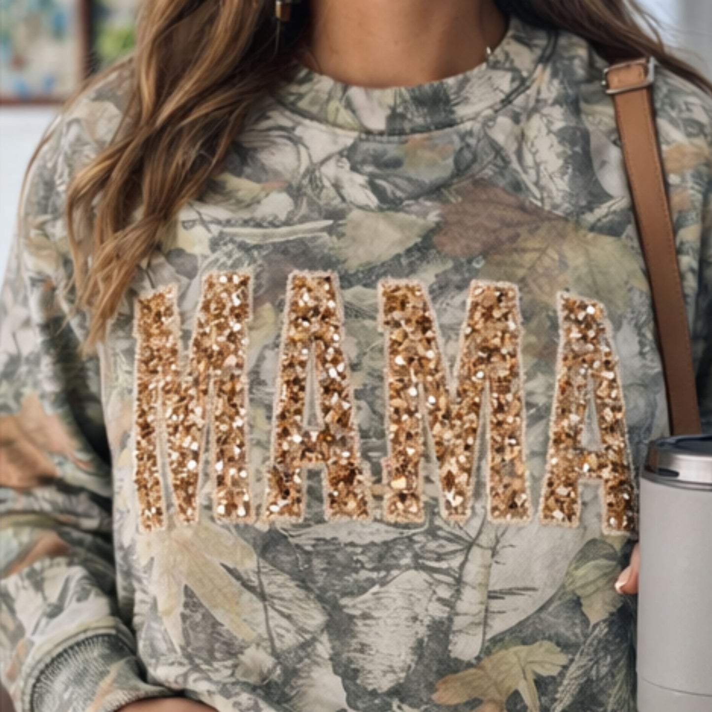 Camouflage sweatshirt with 'MAMA' in gold sequins worn by a person.