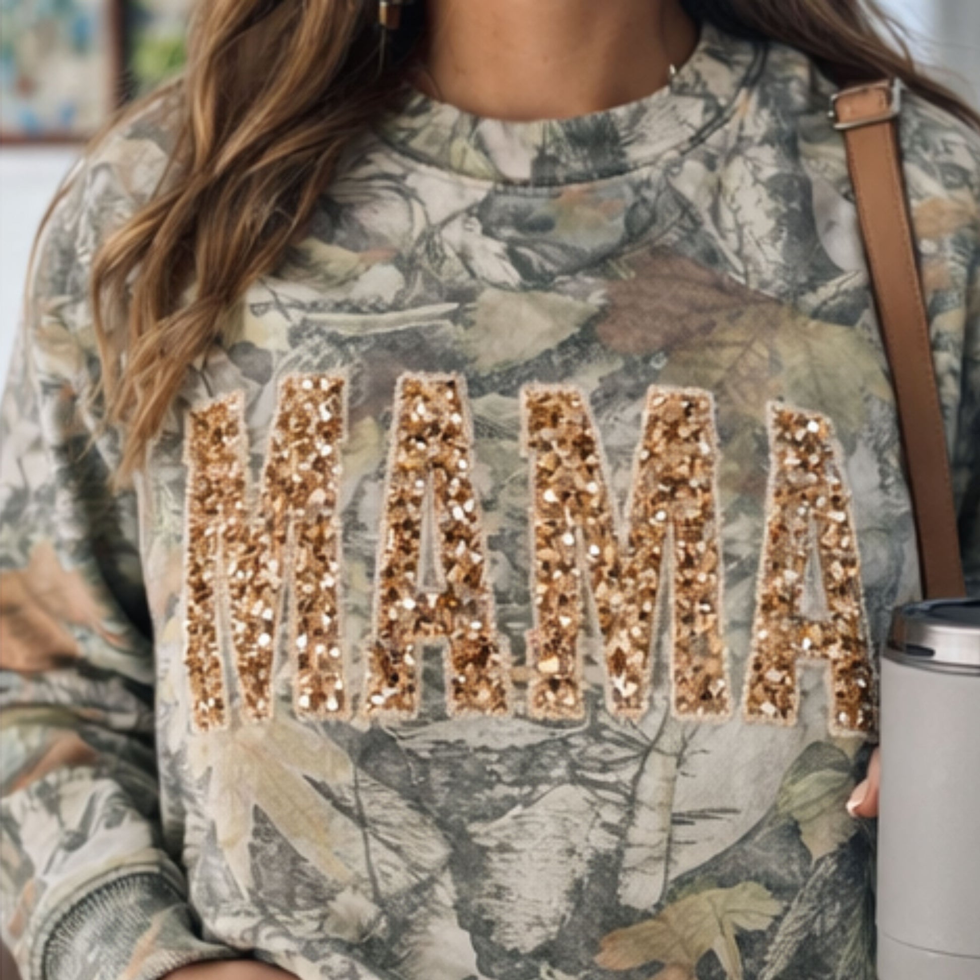 Camouflage sweatshirt with 'MAMA' in gold sequins worn by a person.