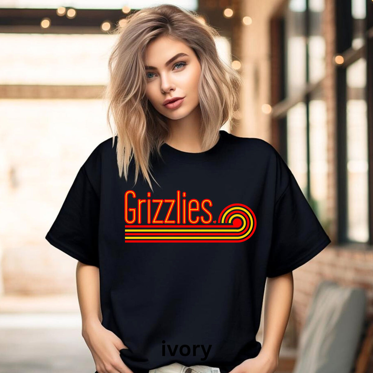 A woman wearing a black oversized T-shirt with a retro-style red and orange 'Grizzlies' graphic across the chest, standing in a softly blurred indoor setting with warm lights and brick walls.