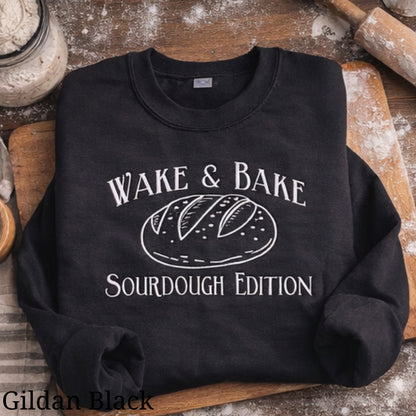 Black sweatshirt with 'Wake & Bake Sourdough Edition' text and bread graphic on a rustic background.