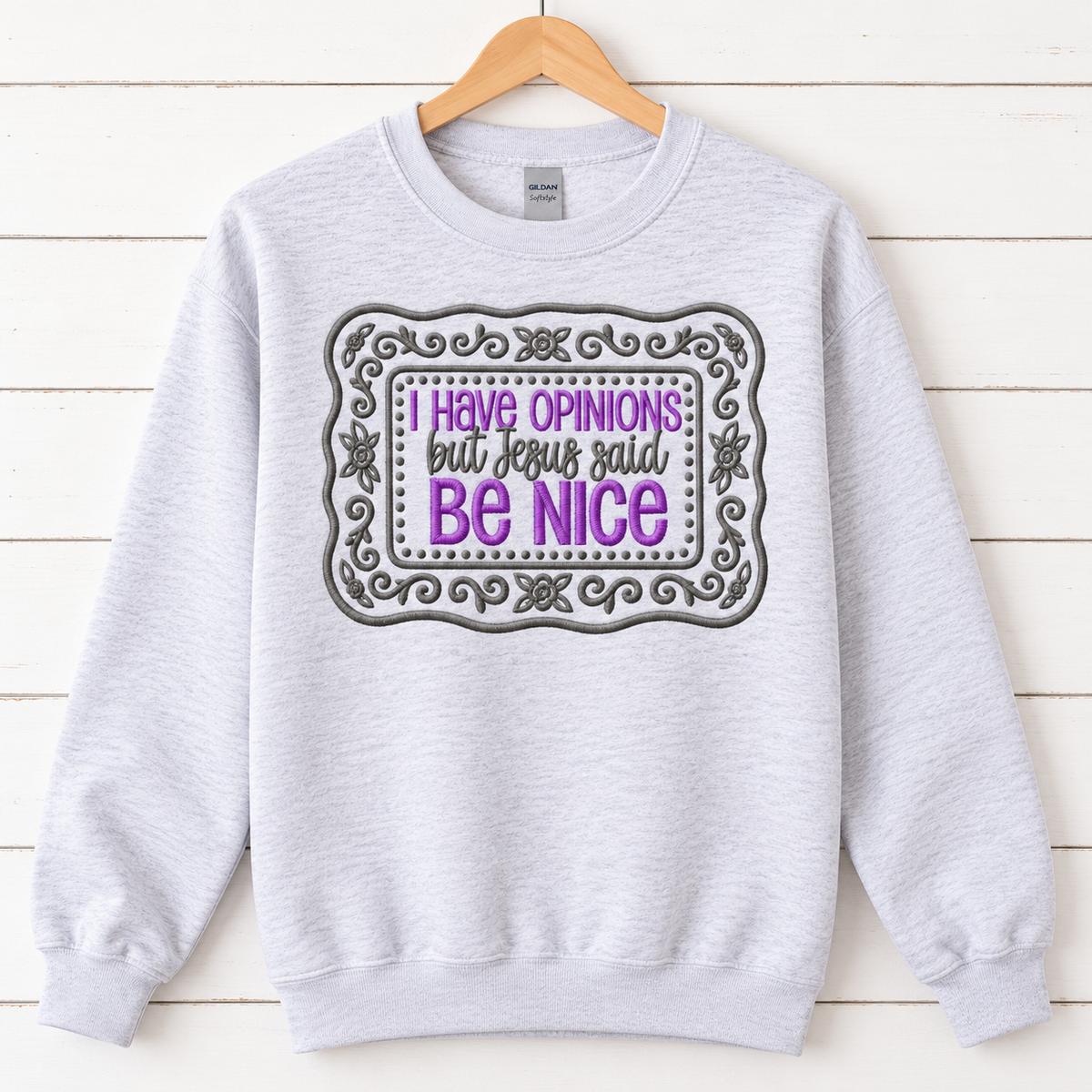 Ash Gildan Softstyle embroidered Be Nice sweatshirt on a natural wood hanger
