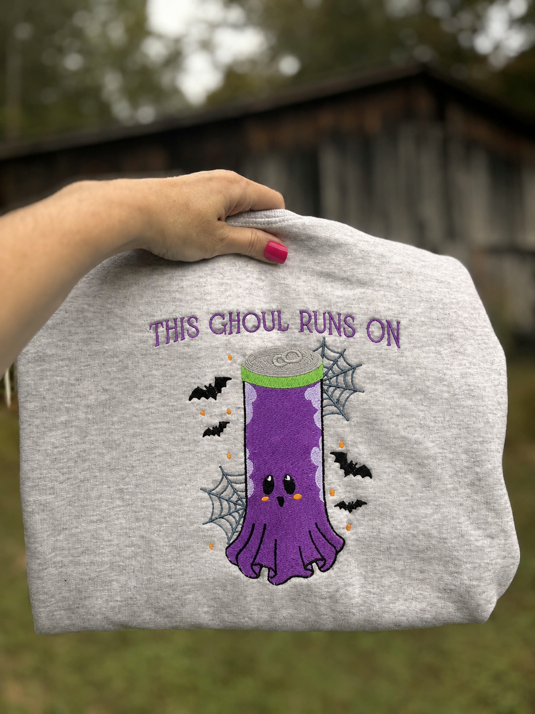 Folded Ash ghost can Halloween embroidered sweatshirt held outdoors