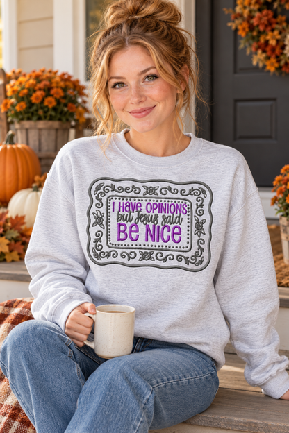 Woman in Ash embroidered Jesus Said Be Nice sweatshirt holding coffee on a fall porch