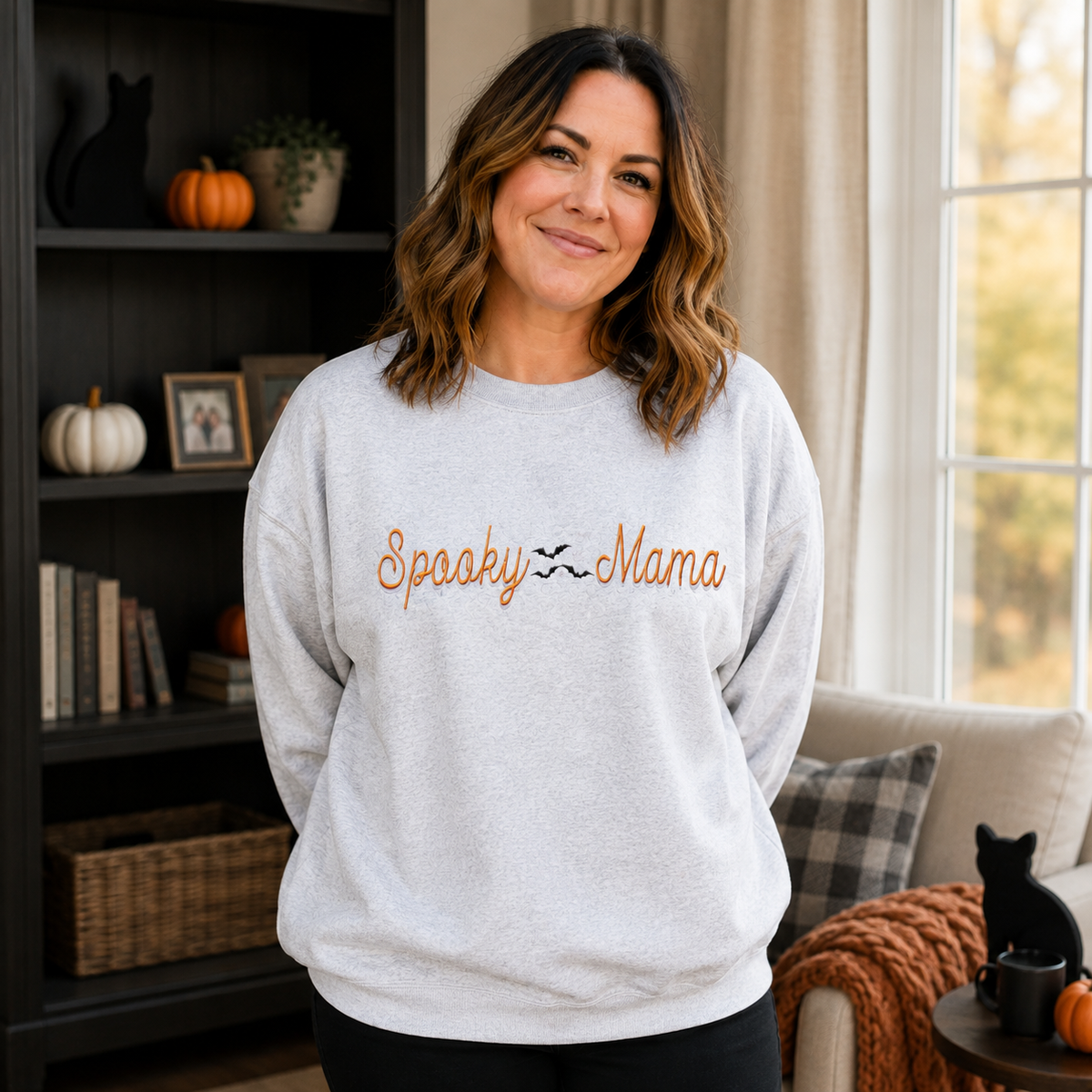 Woman wearing Ash Spooky Mama embroidered sweatshirt in a cozy Halloween home