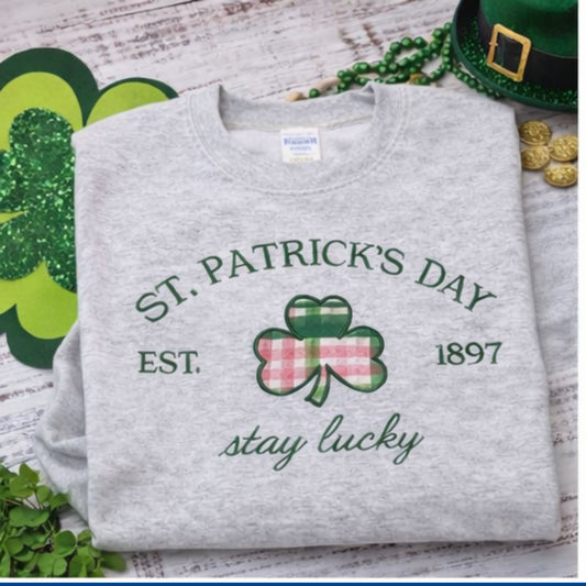 Gray sweatshirt with St. Patrick's Day design featuring a shamrock and text on a wooden surface with festive items.