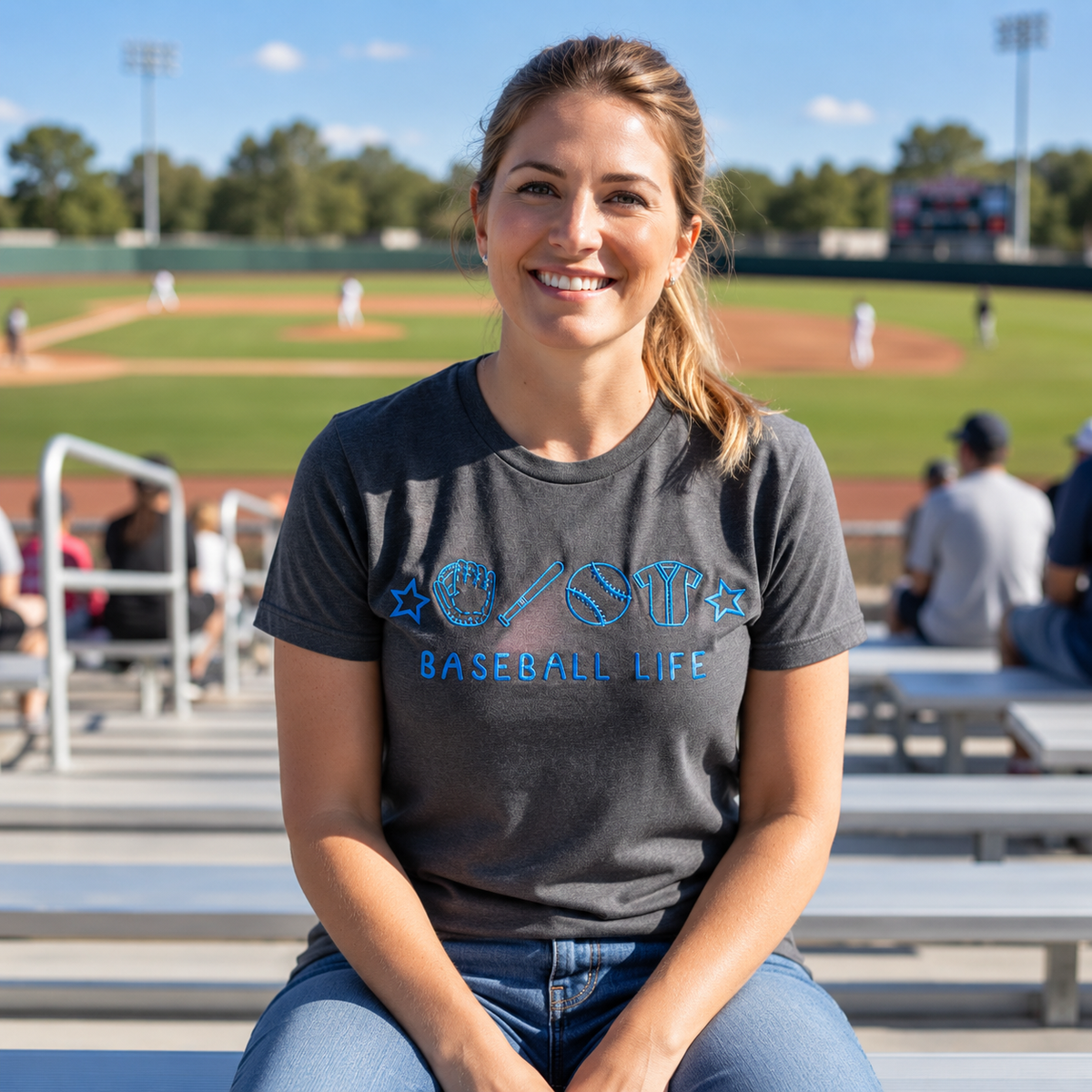 Woman wearing a charcoal Baseball Life embroidered Comfort Colors shirt at a baseball field
