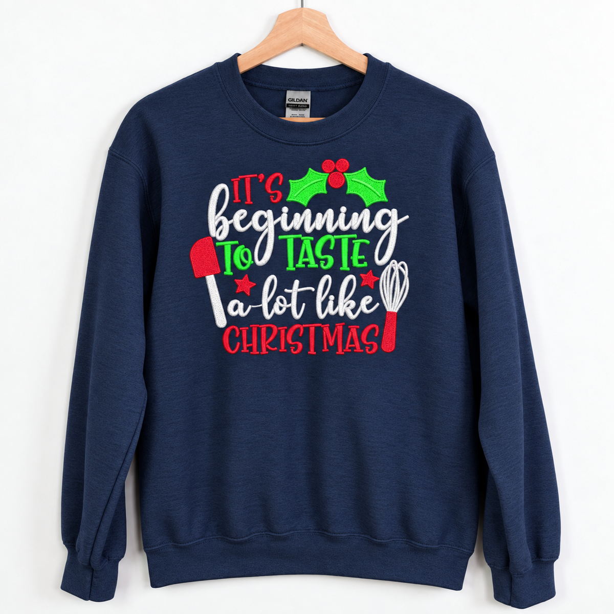 Navy Christmas baking embroidered Gildan crewneck on a wooden hanger
