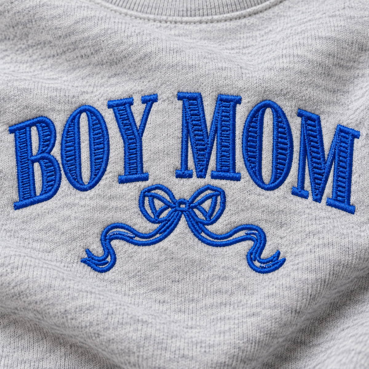 Close-up of royal blue Boy Mom bow embroidery stitched on Ash heather sweatshirt fleece
