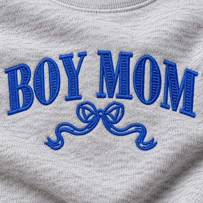 Close-up of royal blue Boy Mom bow embroidery stitched on Ash heather sweatshirt fleece