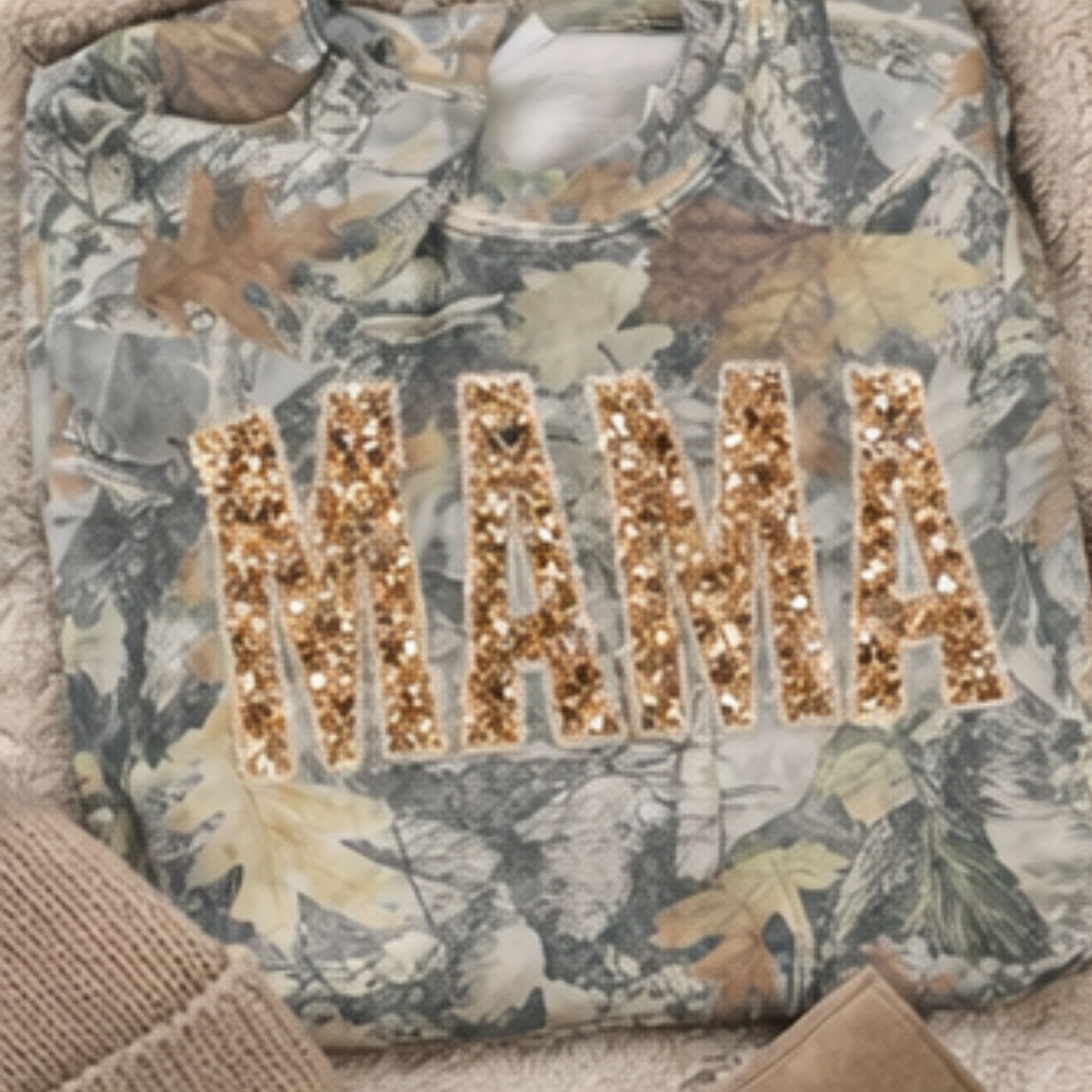 Camouflage shirt with 'MAMA' in gold sequin letters on a textured surface