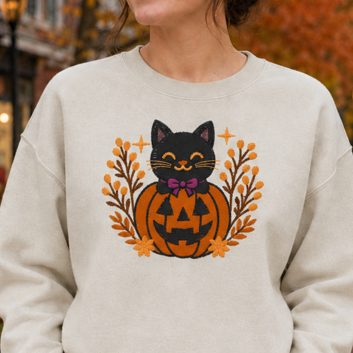 Close-up of the exact black cat jack-o-lantern embroidery on a Sand crewneck sweatshirt