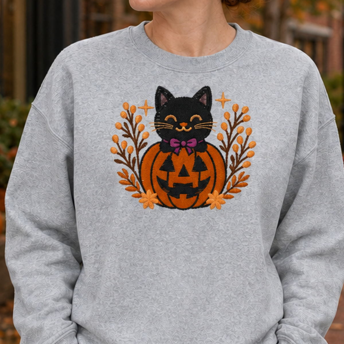 Close-up of the exact black cat jack-o-lantern embroidery on a Sport Grey crewneck sweatshirt