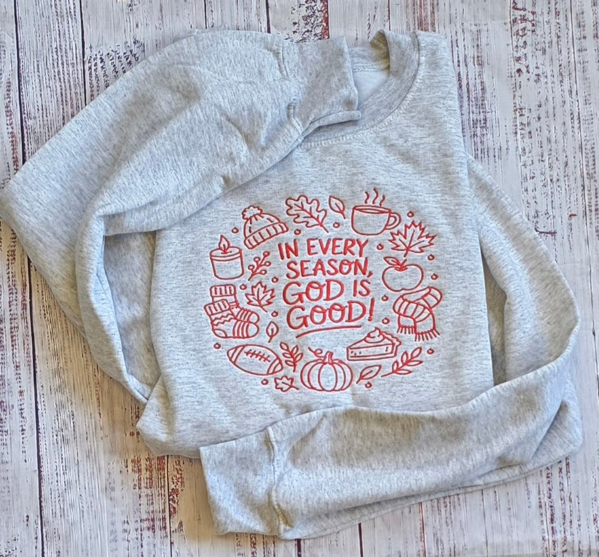 Christian fall embroidered Ash sweatshirt arranged flat with In Every Season God Is Good design