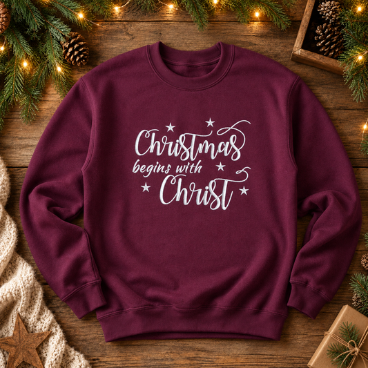 Maroon Christmas Begins With Christ embroidered crewneck sweatshirt in a rustic holiday flat lay