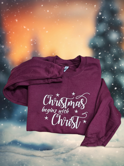 Real Christmas Begins With Christ white embroidery on a Maroon crewneck sweatshirt