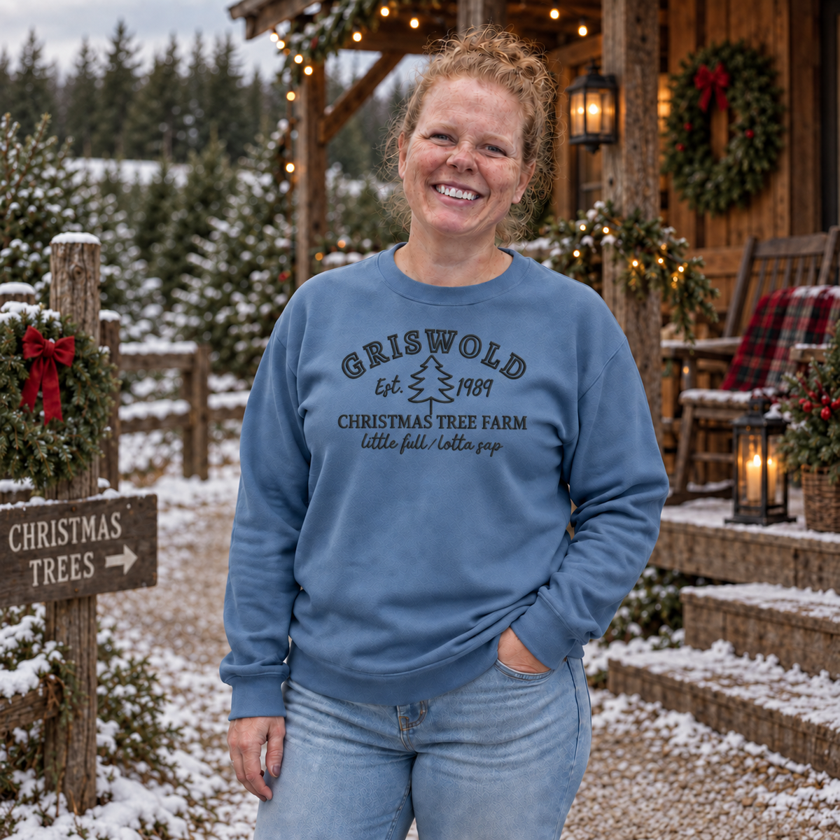 Stone blue Christmas tree farm sweatshirt with dark embroidered thread near a decorated winter cabin