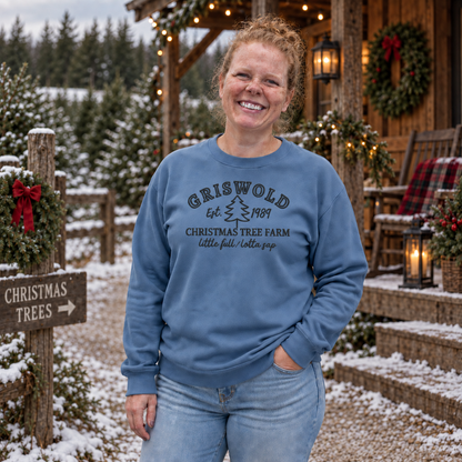 Stone blue Christmas tree farm sweatshirt with dark embroidered thread near a decorated winter cabin