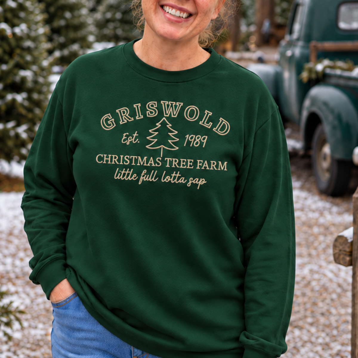Close view of cream Christmas tree farm embroidery on a forest green crewneck sweatshirt