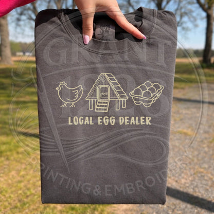 Folded t-shirt with embroidered 'Local Egg Dealer' design 