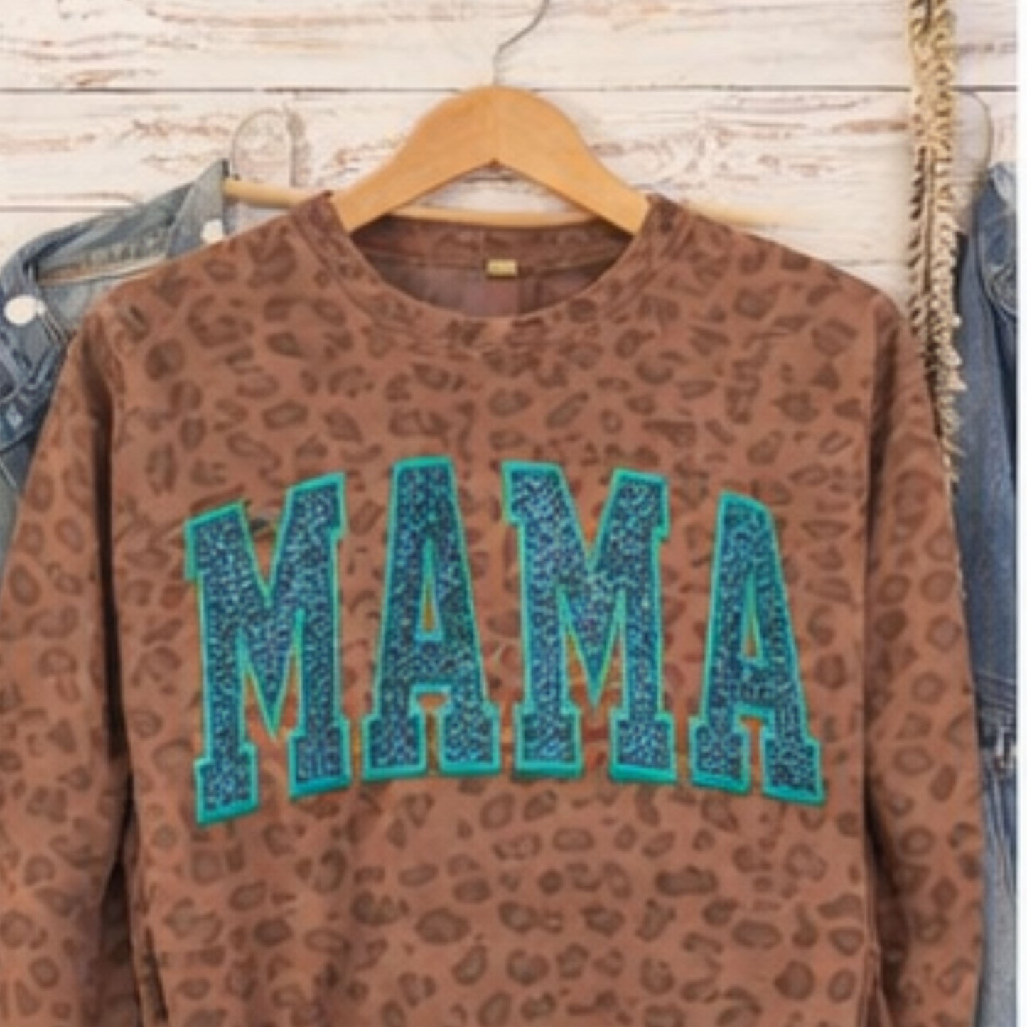 Brown leopard print sweatshirt with 'MAMA' in blue letters on a wooden surface.