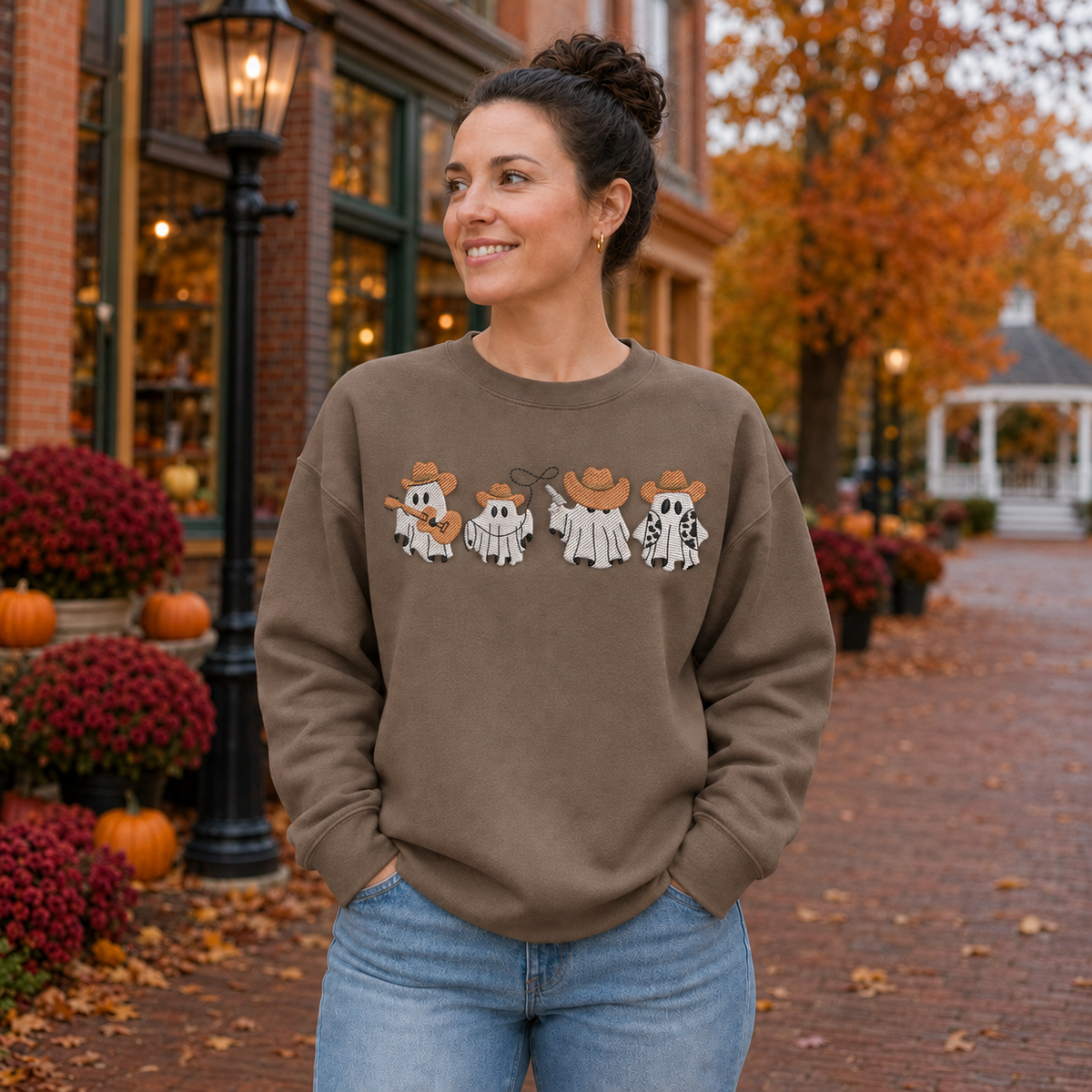 Woman wearing a Brown Savanna embroidered sweatshirt with four cowboy ghosts in an autumn town setting