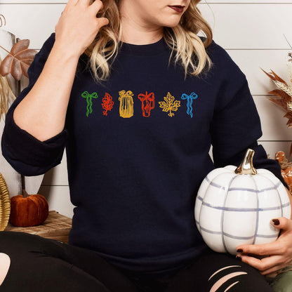 Navy sweatshirt with colorful embroidered fall icons modeled with a white pumpkin