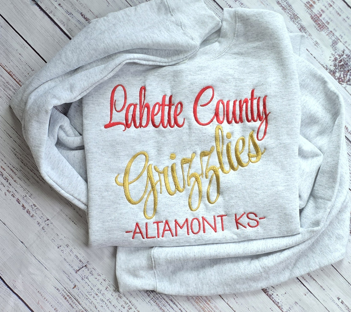 Ash sweatshirt showing three-line custom school spirit embroidery