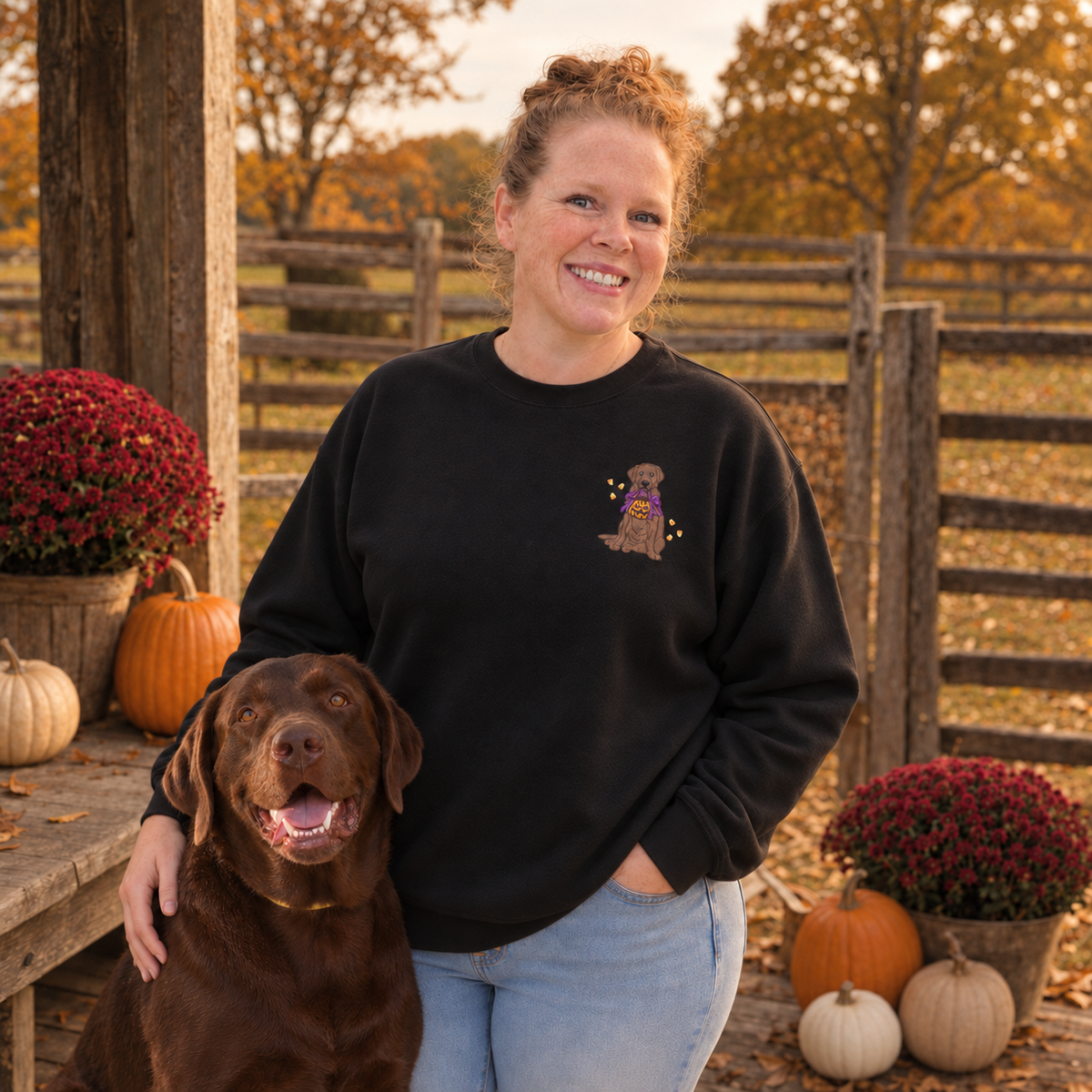 Woman with chocolate Labrador wearing a black embroidered Halloween Lab sweatshirt on a fall porch