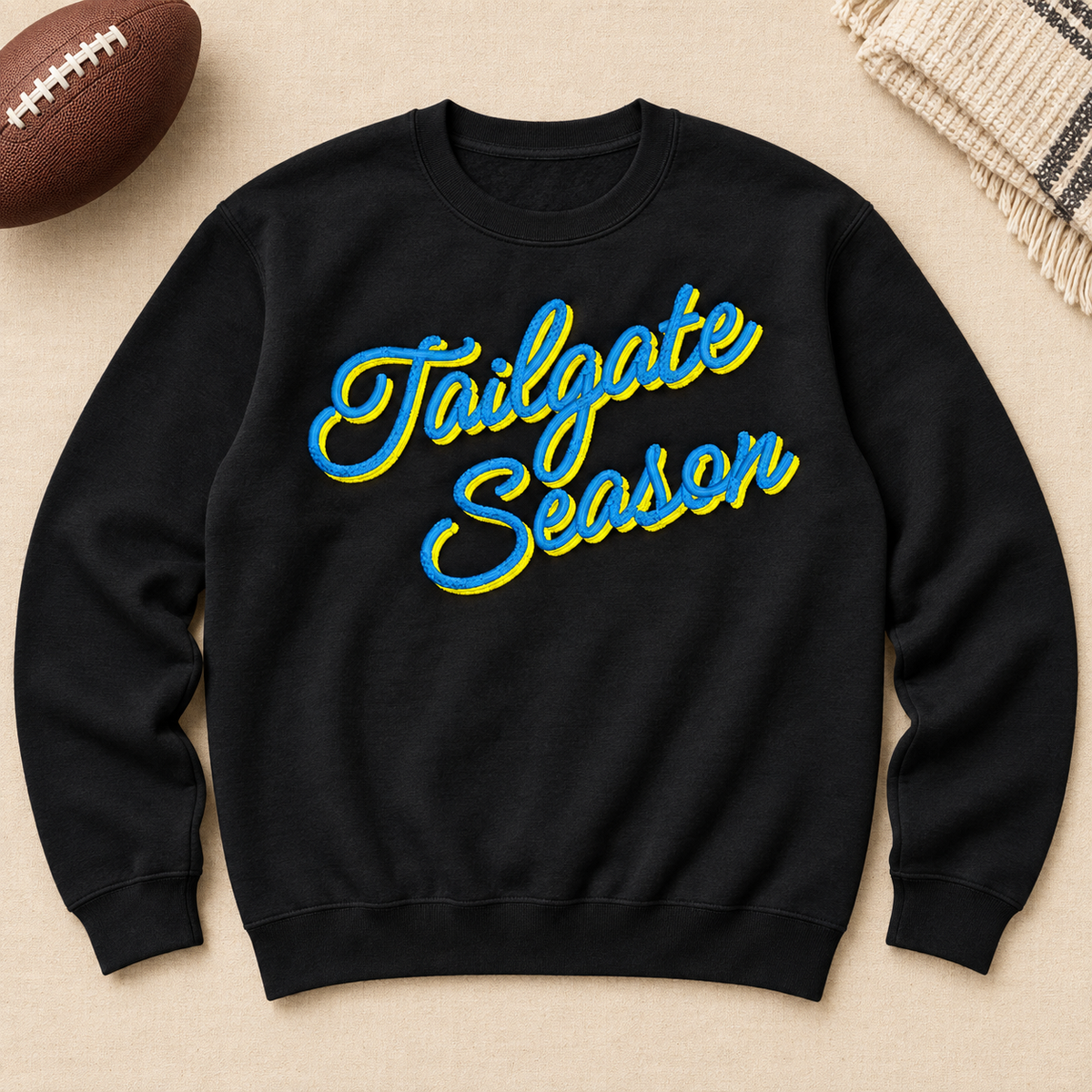 Black crewneck sweatshirt flat lay featuring the angled Tailgate Season embroidery in blue and yellow