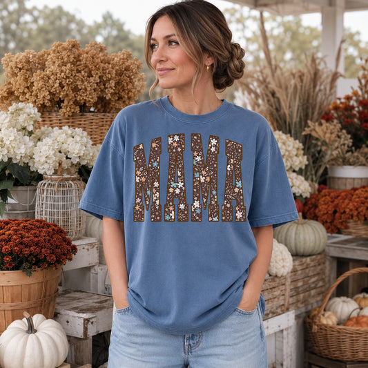 Woman wearing a Blue Jean Comfort Colors shirt with a brown floral varsity MAMA graphic in a fall setting