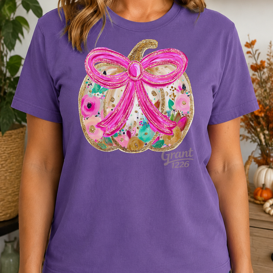 Woman wearing violet Comfort Colors floral pumpkin shirt with a large pink bow